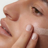 Close-up of a model blending Dr Hauschka Illuminating Fluid 30ml across her cheek for a luminous finish.