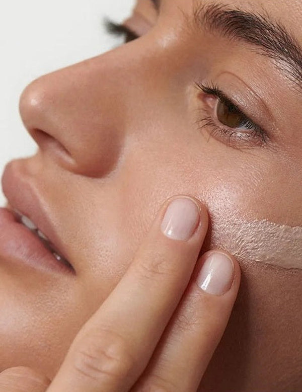 Close-up of a model blending Dr Hauschka Illuminating Fluid 30ml across her cheek for a luminous finish.