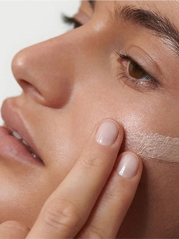Close-up of a model blending Dr Hauschka Illuminating Fluid 30ml across her cheek for a luminous finish.