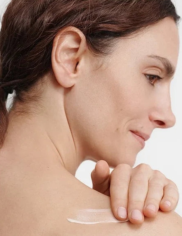 Woman smoothing a white streak of Dr Hauschka Regenerating Body Cream 150ml across her bare shoulder with her fingertips.
