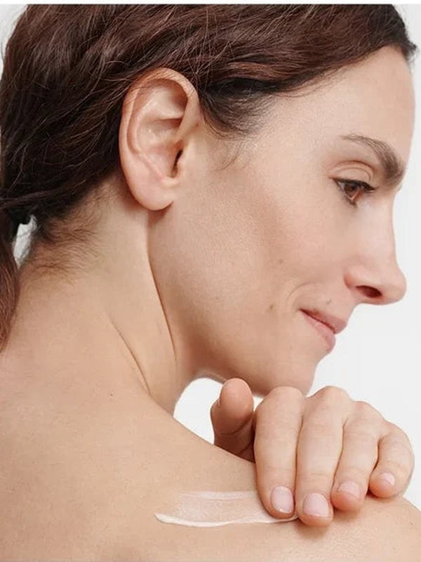 Woman smoothing a white streak of Dr Hauschka Regenerating Body Cream 150ml across her bare shoulder with her fingertips.