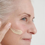 Grey-haired woman applying a thick ivory streak of Dr Hauschka Regenerating Day Cream Intensive 40ml across her cheek.
