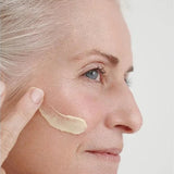 Grey-haired woman applying a thick ivory streak of Dr Hauschka Regenerating Day Cream Intensive 40ml across her cheek.