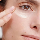 Close-up of a woman smoothing Dr Hauschka Regenerating Eye Cream 15ml beneath her eye with two fingertips.