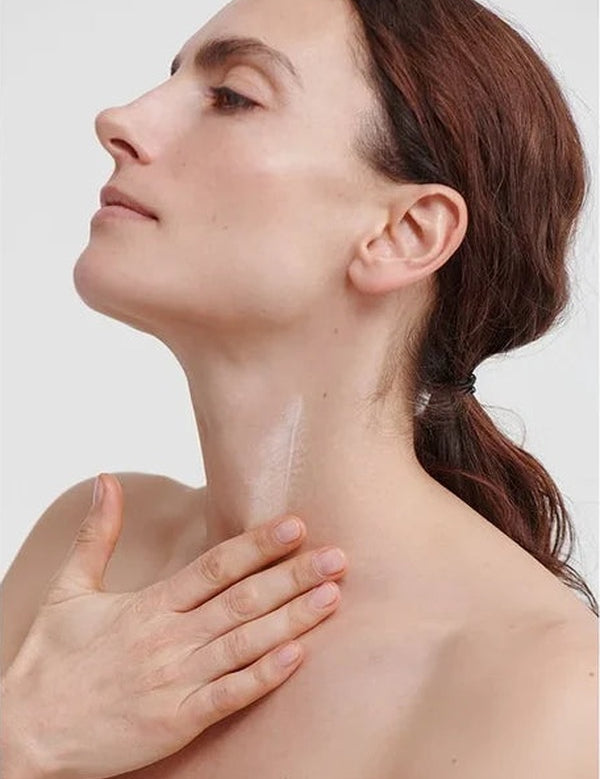 Woman massaging Dr Hauschka Regenerating Neck and Décolleté Cream 40ml into the front of her neck with her chin gently raised.