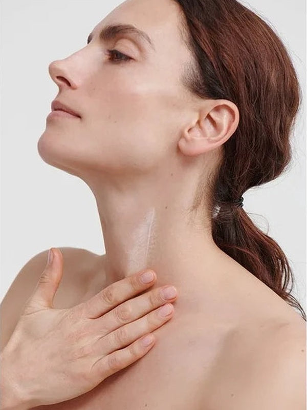 Woman massaging Dr Hauschka Regenerating Neck and Décolleté Cream 40ml into the front of her neck with her chin gently raised.