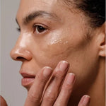 Close-up of a woman applying a glossy streak of Dr Hauschka Regenerating Night Serum Intensive to her cheek with her fingertips.