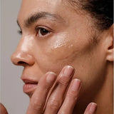 Close-up of a woman applying a glossy streak of Dr Hauschka Regenerating Night Serum Intensive to her cheek with her fingertips.