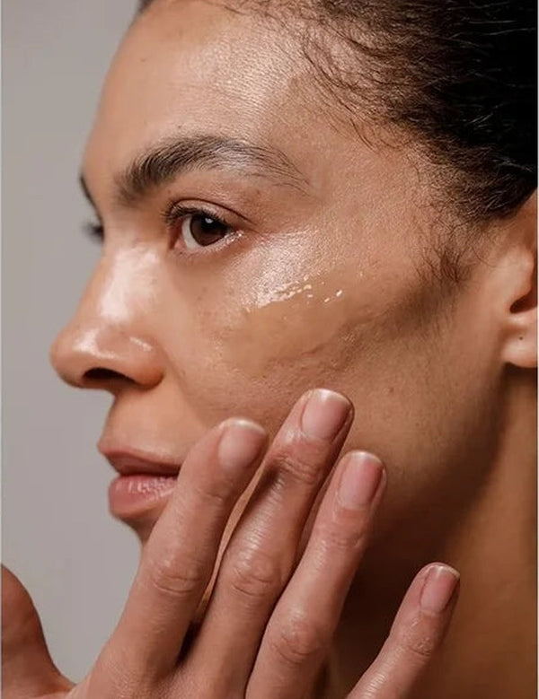 Close-up of a woman applying a glossy streak of Dr Hauschka Regenerating Night Serum Intensive to her cheek with her fingertips.