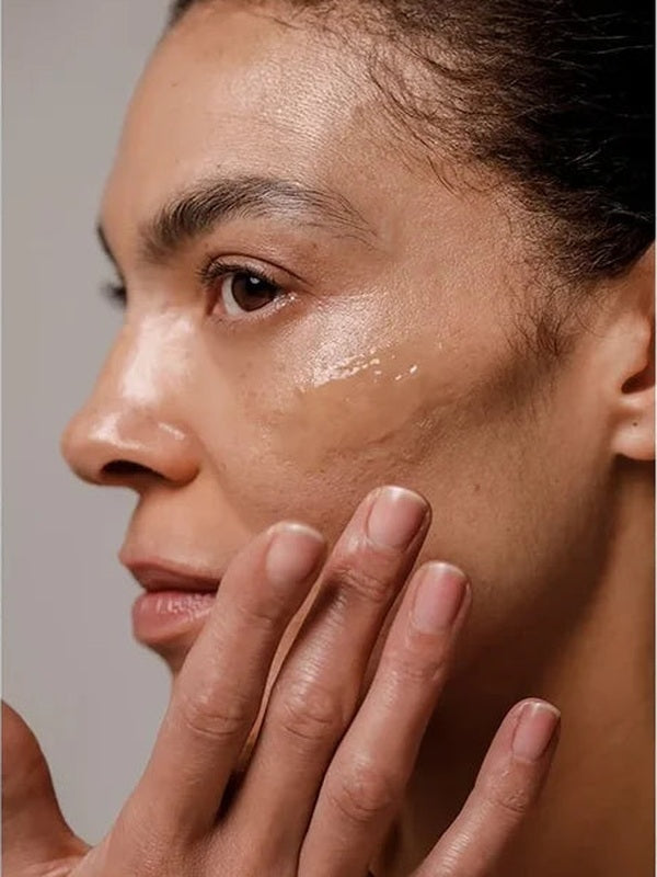Close-up of a woman applying a glossy streak of Dr Hauschka Regenerating Night Serum Intensive to her cheek with her fingertips.