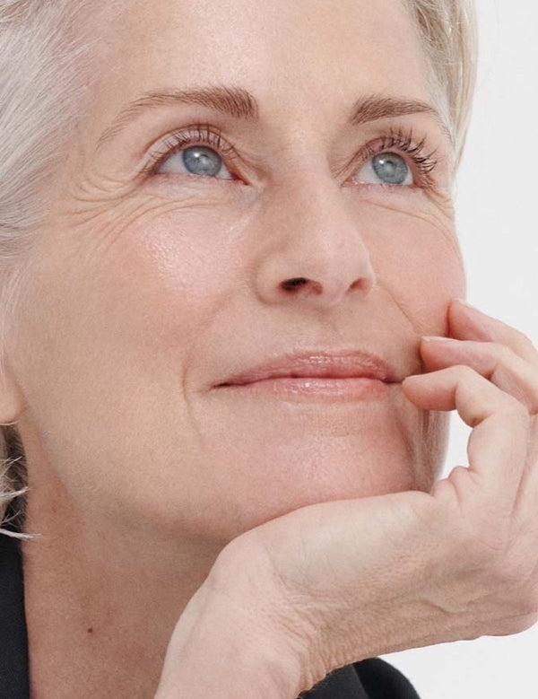 Close-up of a grey-haired woman looking upward with her chin resting on her hand, in the Dr Hauschka Regenerating Oil Serum Intensive photograph.
