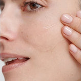 Close-up of a model smoothing a clear streak of Dr Hauschka Regenerating Serum 30ml across her cheek with two fingertips.