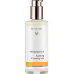 Dr Hauschka Soothing Cleansing Milk in a clear bottle containing ivory lotion, with a reflective metal pump and white label with a golden-yellow band.