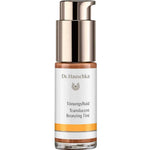A bottle of Dr Hauschka Translucent Bronzing Tint 18ml with a gold pump, white label, and orange accent at the base. The vegan bronzer’s label provides product details in German and English.