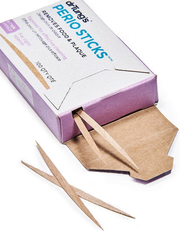 Open white and purple Dr Tung's Perio Sticks carton labelled X-Thin, with slender, pointed wooden dental sticks protruding from the opening and lying beside it.