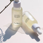 Two frosted bottles of Ere Perez Australian Blue Cypress Face Nectar with a cypress sprig on a cream background