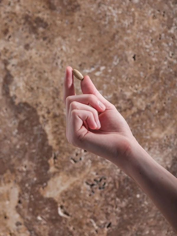 Hand holding a single Herbs of Gold Clear Skin tablet