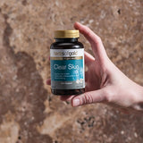 Hand holding the Herbs of Gold Clear Skin bottle against a stone background