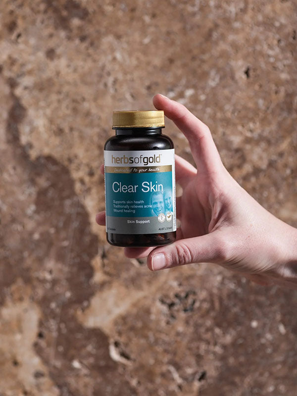 Hand holding the Herbs of Gold Clear Skin bottle against a stone background