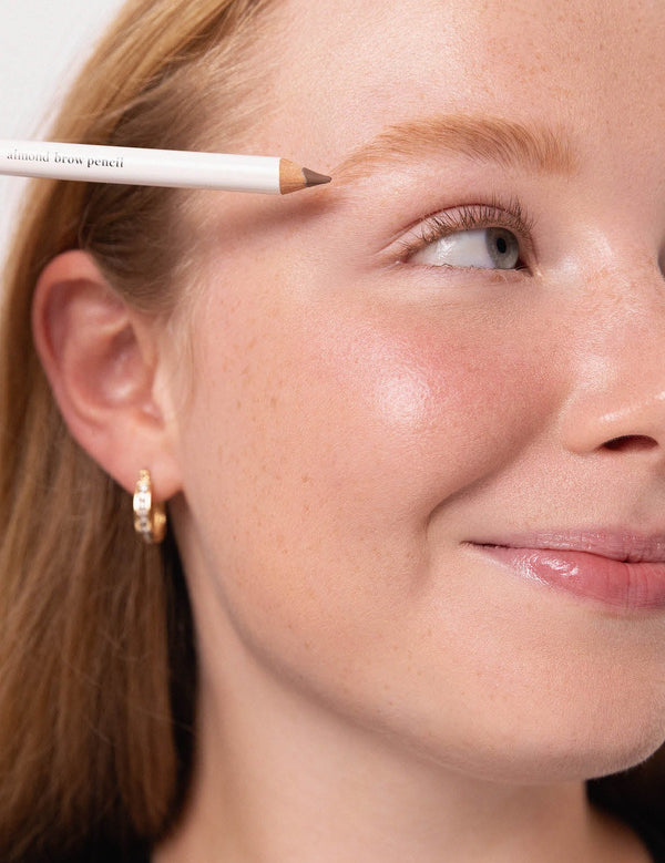 Model positioning an Ere Perez Almond Brow Pencil above her eyebrow to define the brow shape.