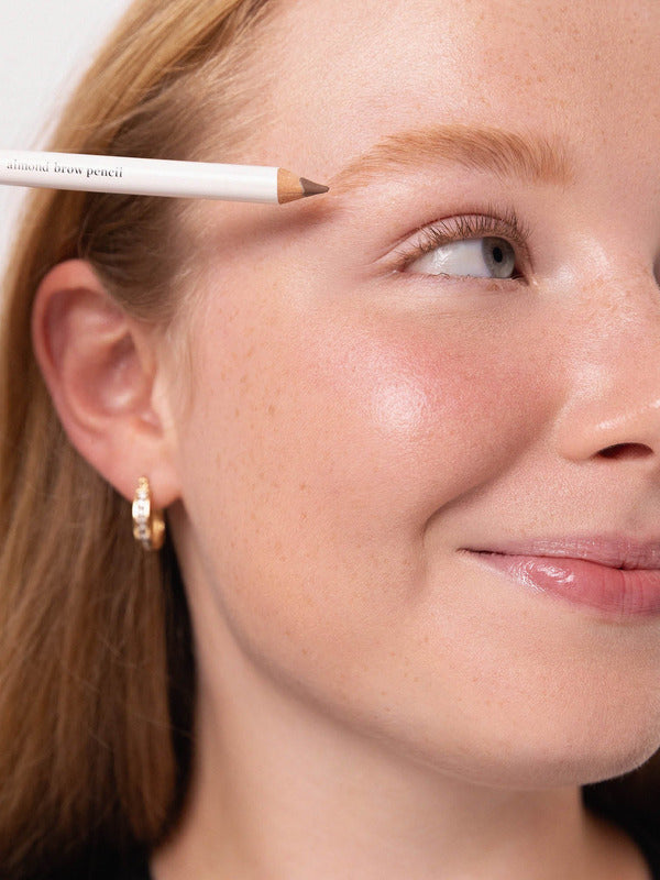 Model positioning an Ere Perez Almond Brow Pencil above her eyebrow to define the brow shape.