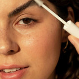 Close-up of a woman grooming her eyebrow with the white brush from Ere Perez Aloe Gel Lash & Brow Mascara Clear.