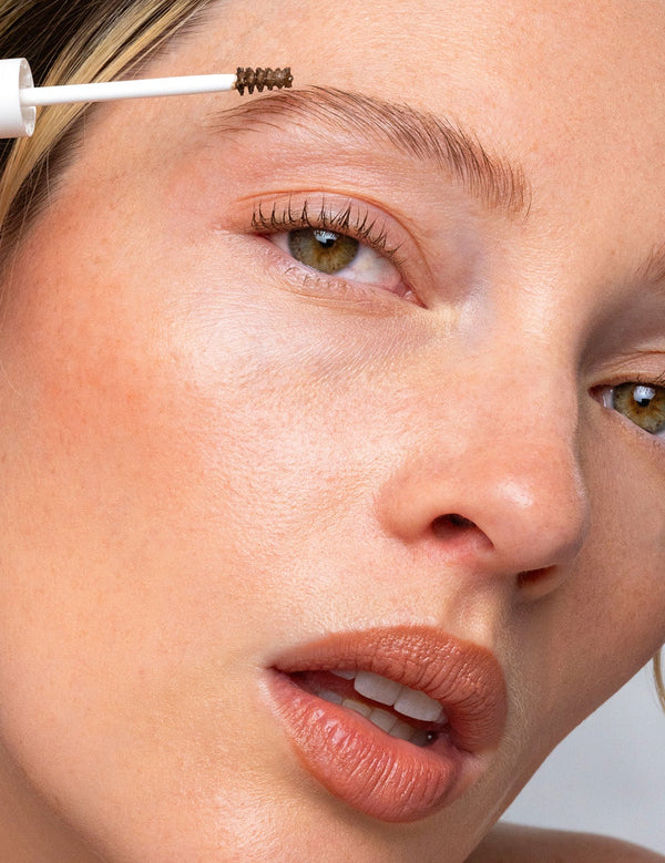 Close-up of a model applying Ere Perez Argan Brow Hero to shape and groom the eyebrow.