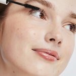 Model applying Ere Perez Avocado Waterproof Mascara to her upper lashes with the mascara wand.