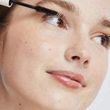 Model applying Ere Perez Avocado Waterproof Mascara to her upper lashes with the mascara wand.