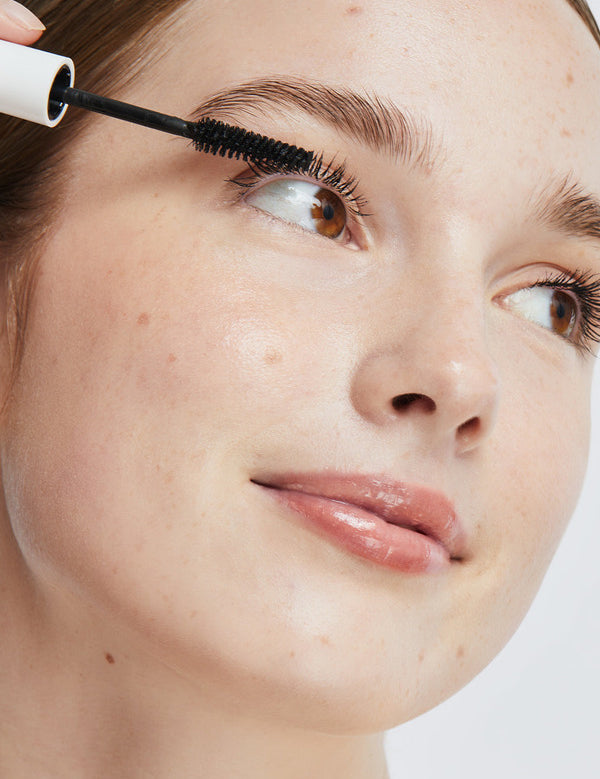 Model applying Ere Perez Avocado Waterproof Mascara to her upper lashes with the mascara wand.