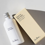 Ere Perez Black Tea Face Toner white bottle and cream carton arranged diagonally on a pale grey surface, with silver cap, printed labels and strong shadows visible.
