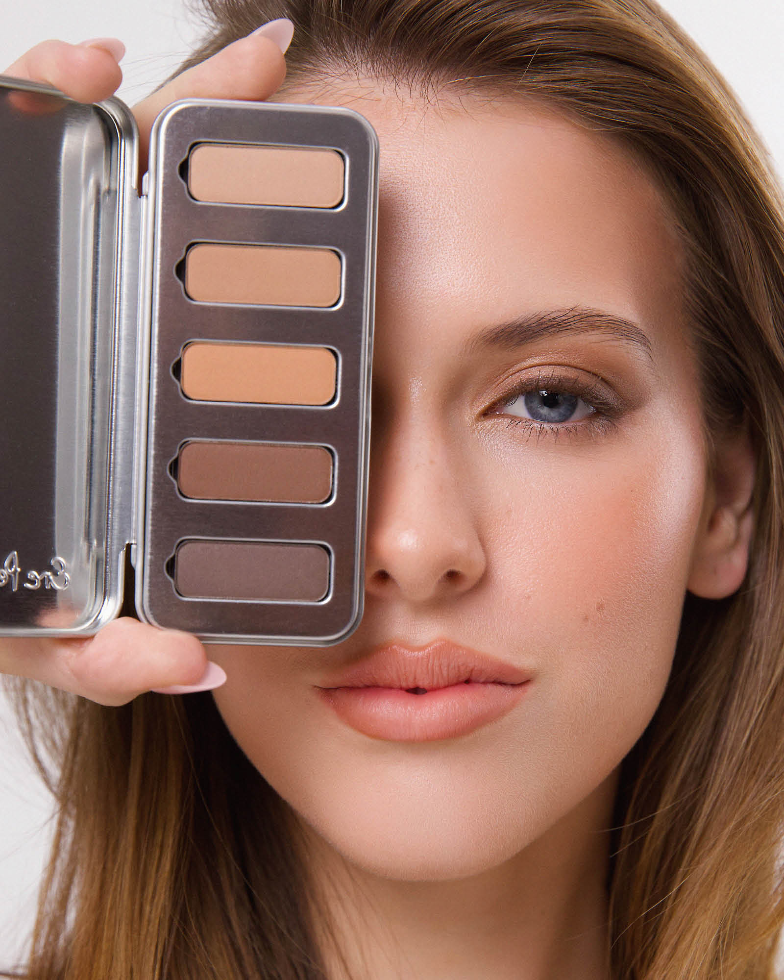 Model holding the open Ere Perez Element Matte Chamomile Eye Palette beside her face, with five neutral shades visible and softly blended brown eyeshadow on the exposed eye.