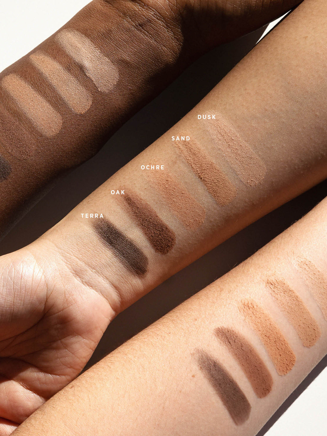 Ere Perez Element Matte eyeshadow swatches across three forearms with light, medium and deep skin tones. The five matte shades are labelled Dusk, Sand, Ochre, Oak and Terra.