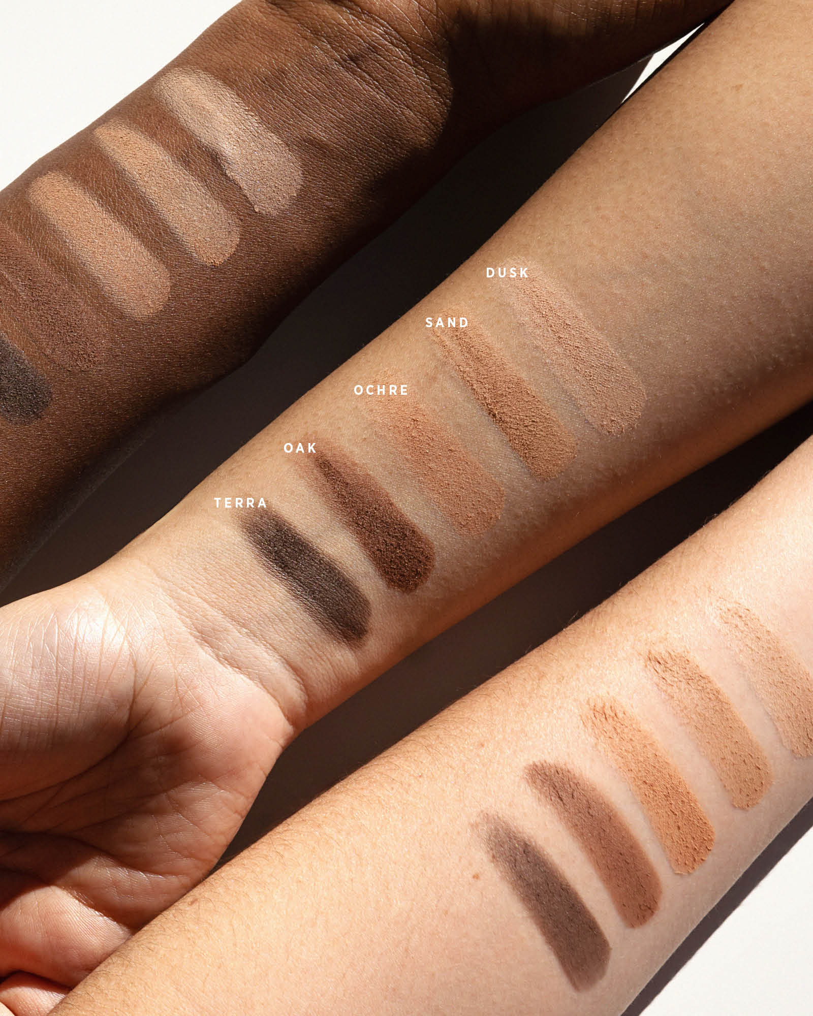 Ere Perez Element Matte eyeshadow swatches across three forearms with light, medium and deep skin tones. The five matte shades are labelled Dusk, Sand, Ochre, Oak and Terra.