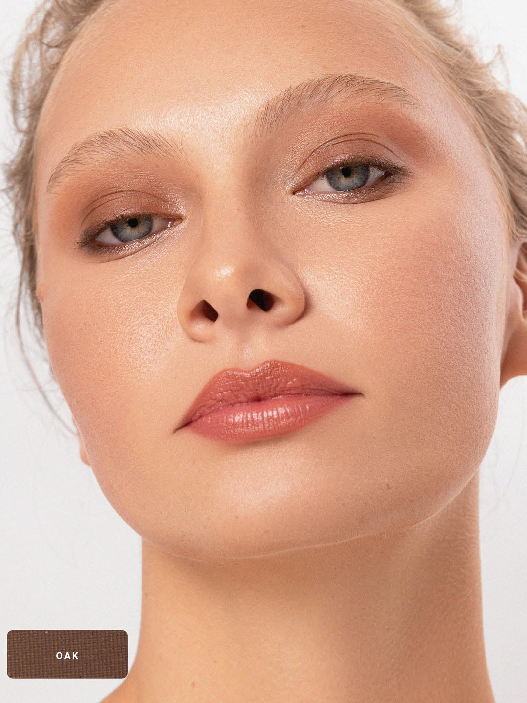 Close-up of a model wearing the earthy brown Oak shade from the Ere Perez Element Matte palette, blended over the eyelids and beneath the lower lashes. An Oak swatch appears at the lower left.