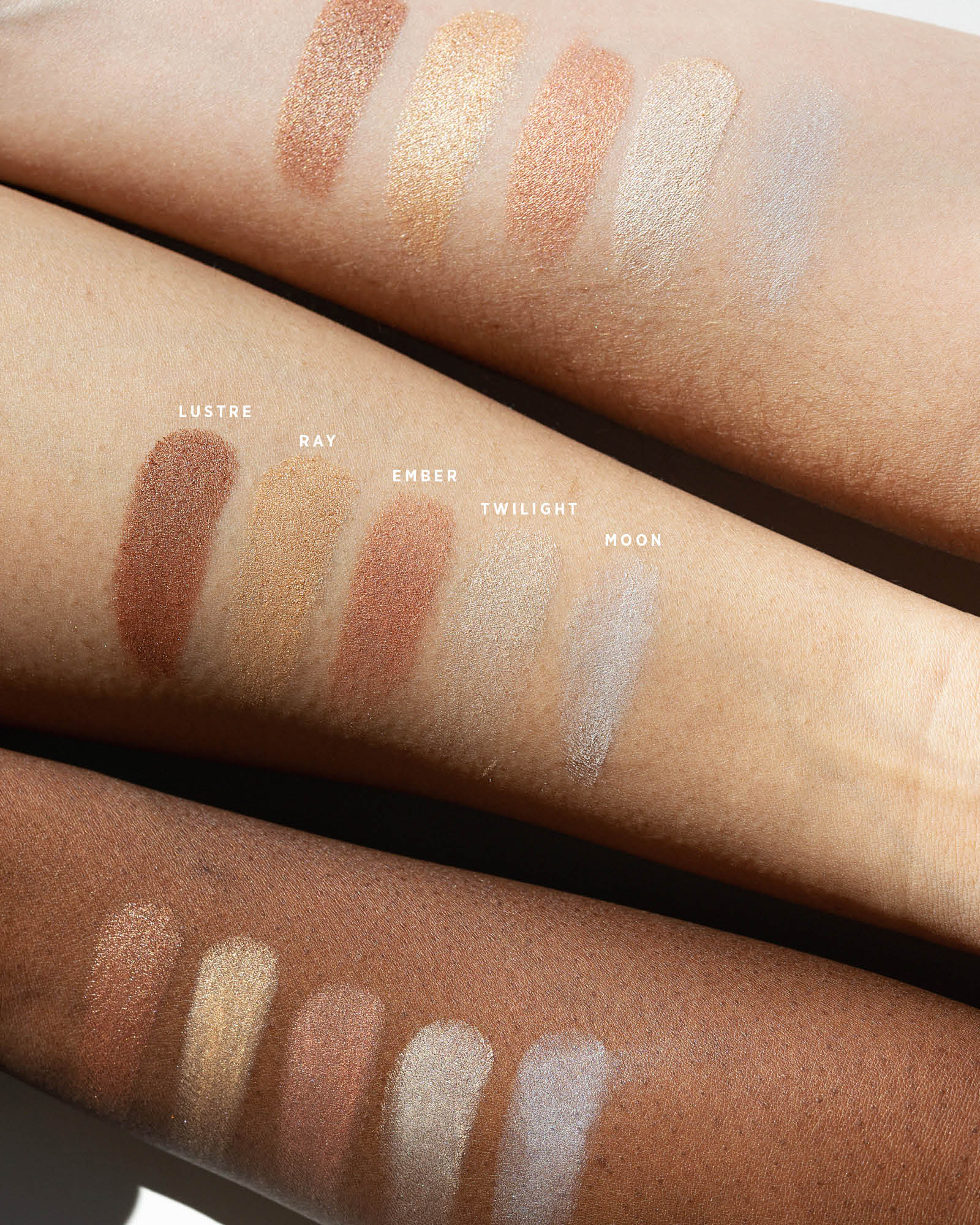 Ere Perez Light Shimmer eyeshadow swatches on three forearms with light, medium and deep skin tones. Lustre, Ray, Ember, Twilight and Moon show bronze, gold, rosy copper, pearl and cool silver finishes.