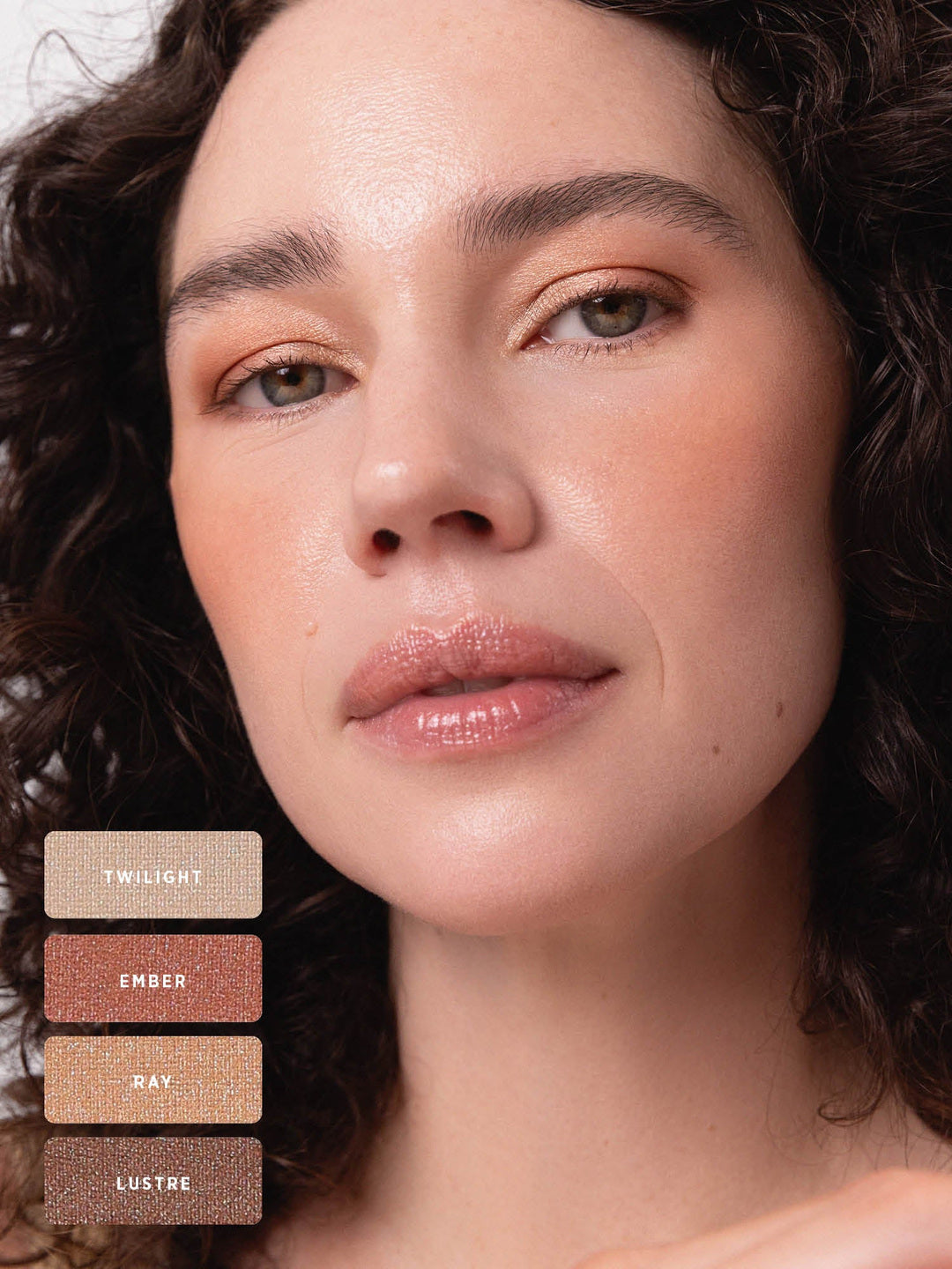 Curly-haired model wearing warm peach and bronze shimmer on the eyelids. Swatches identify Twilight, Ember, Ray and Lustre from the Ere Perez Light Shimmer palette.