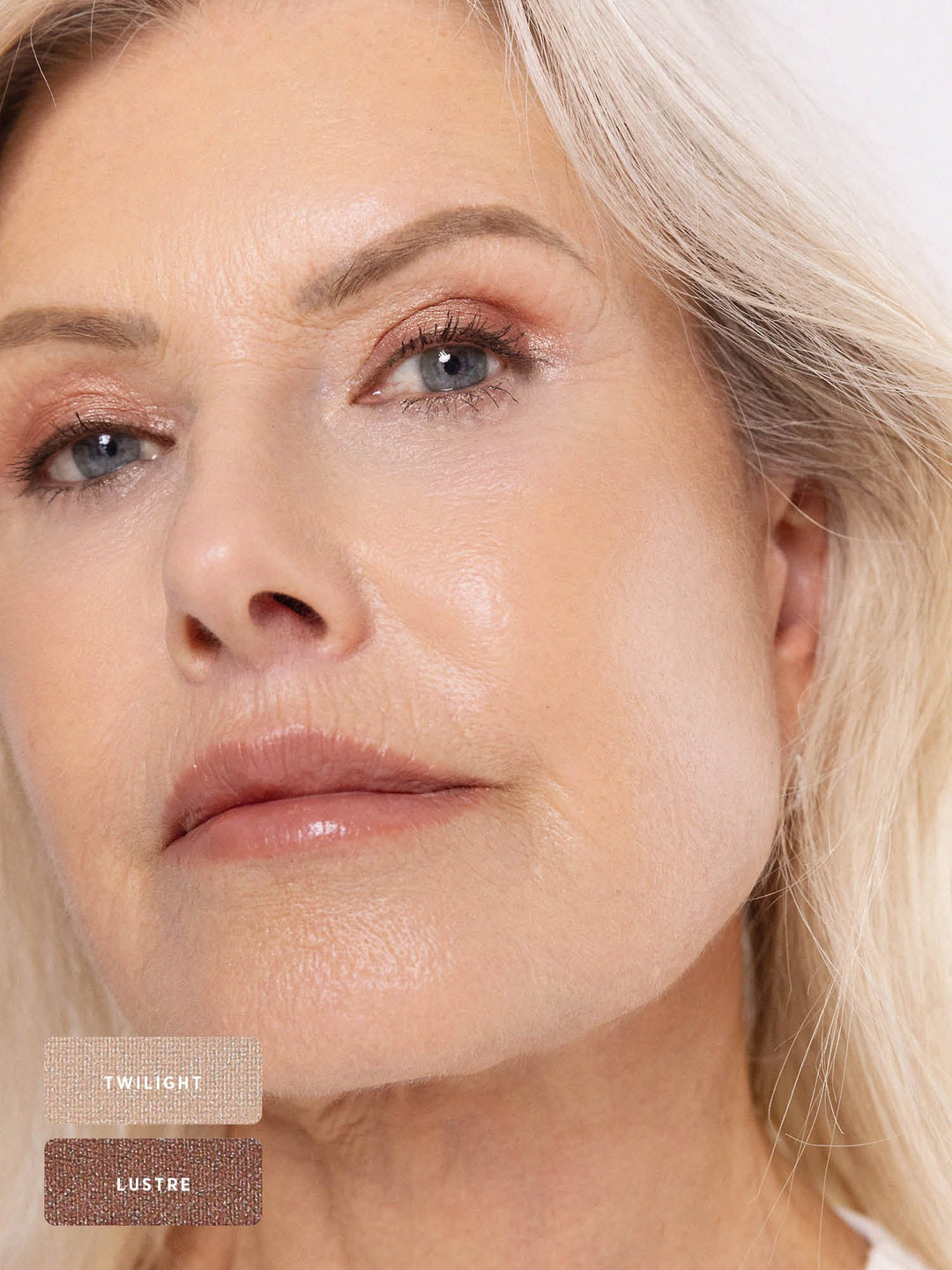 Close-up of a silver-haired model wearing softly blended rose-bronze shimmer on the eyelids. Twilight and Lustre swatches identify the Ere Perez Light Shimmer palette shades used.