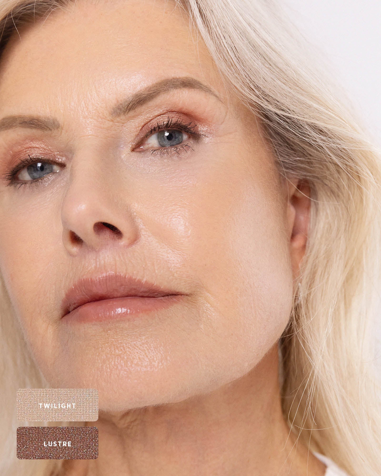 Close-up of a silver-haired model wearing softly blended rose-bronze shimmer on the eyelids. Twilight and Lustre swatches identify the Ere Perez Light Shimmer palette shades used.
