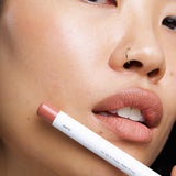 Model wearing Ere Perez Coco Lip & Cheek Crayon with the product held beside her face