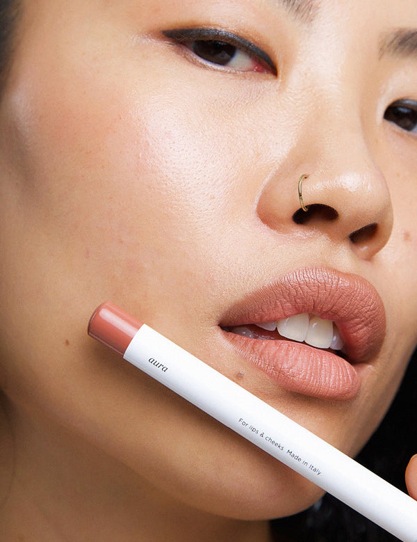 Model wearing Ere Perez Coco Lip & Cheek Crayon with the product held beside her face