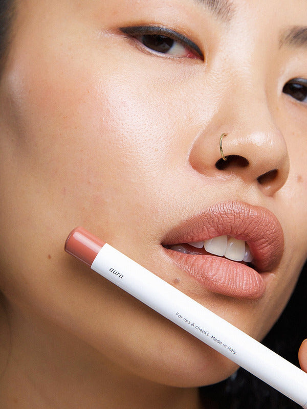 Model wearing Ere Perez Coco Lip & Cheek Crayon with the product held beside her face