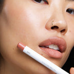 Model wearing Ere Perez Coco Lip & Cheek Crayon with the product held beside her face