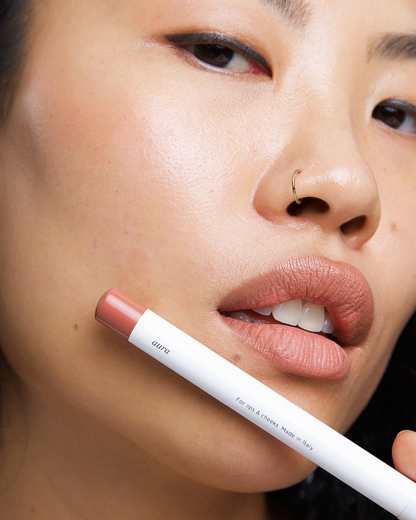 Model wearing Ere Perez Coco Lip & Cheek Crayon with the product held beside her face
