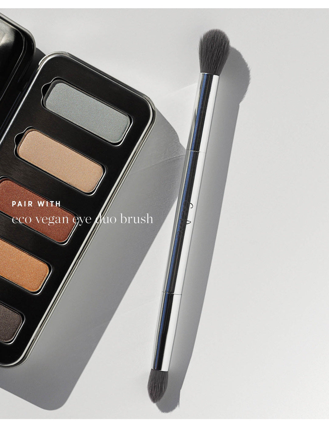 Ere Perez Eco Vegan Eye Duo Brush beside the open Light Shimmer Chamomile Eye Palette. Both dark bristle heads and the silver handle are visible; text reads 'Pair with eco vegan eye duo brush'.