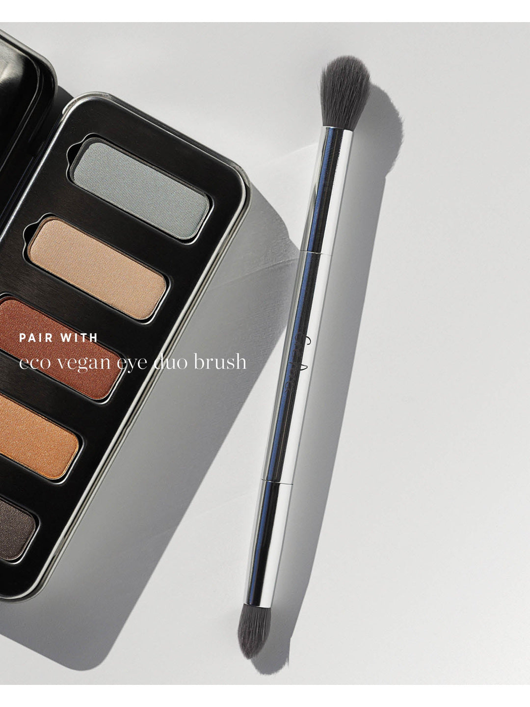Ere Perez Eco Vegan Eye Duo Brush beside the open Light Shimmer Chamomile Eye Palette. Both dark bristle heads and the silver handle are visible; text reads 'Pair with eco vegan eye duo brush'.