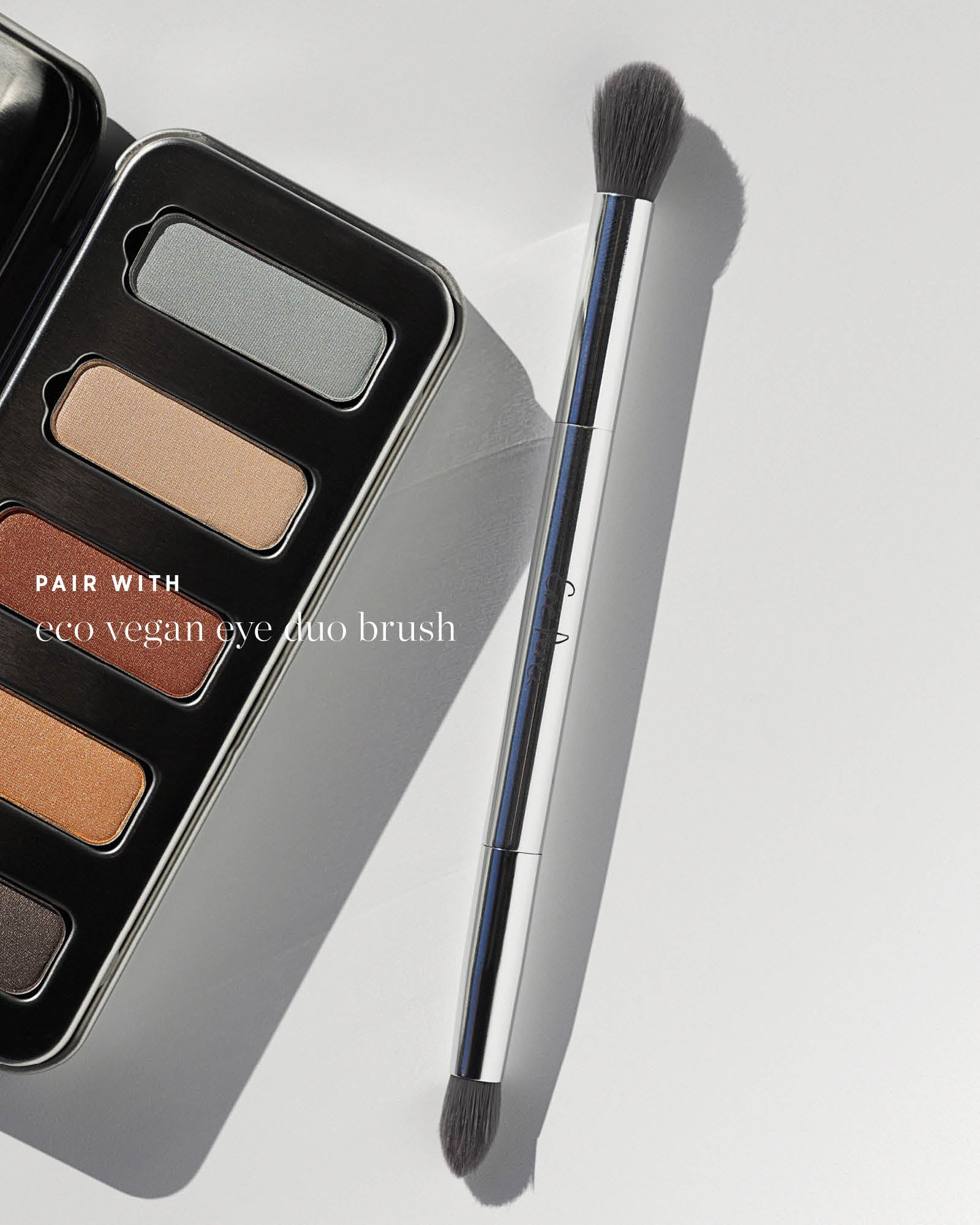 Ere Perez Eco Vegan Eye Duo Brush beside the open Light Shimmer Chamomile Eye Palette. Both dark bristle heads and the silver handle are visible; text reads 'Pair with eco vegan eye duo brush'.