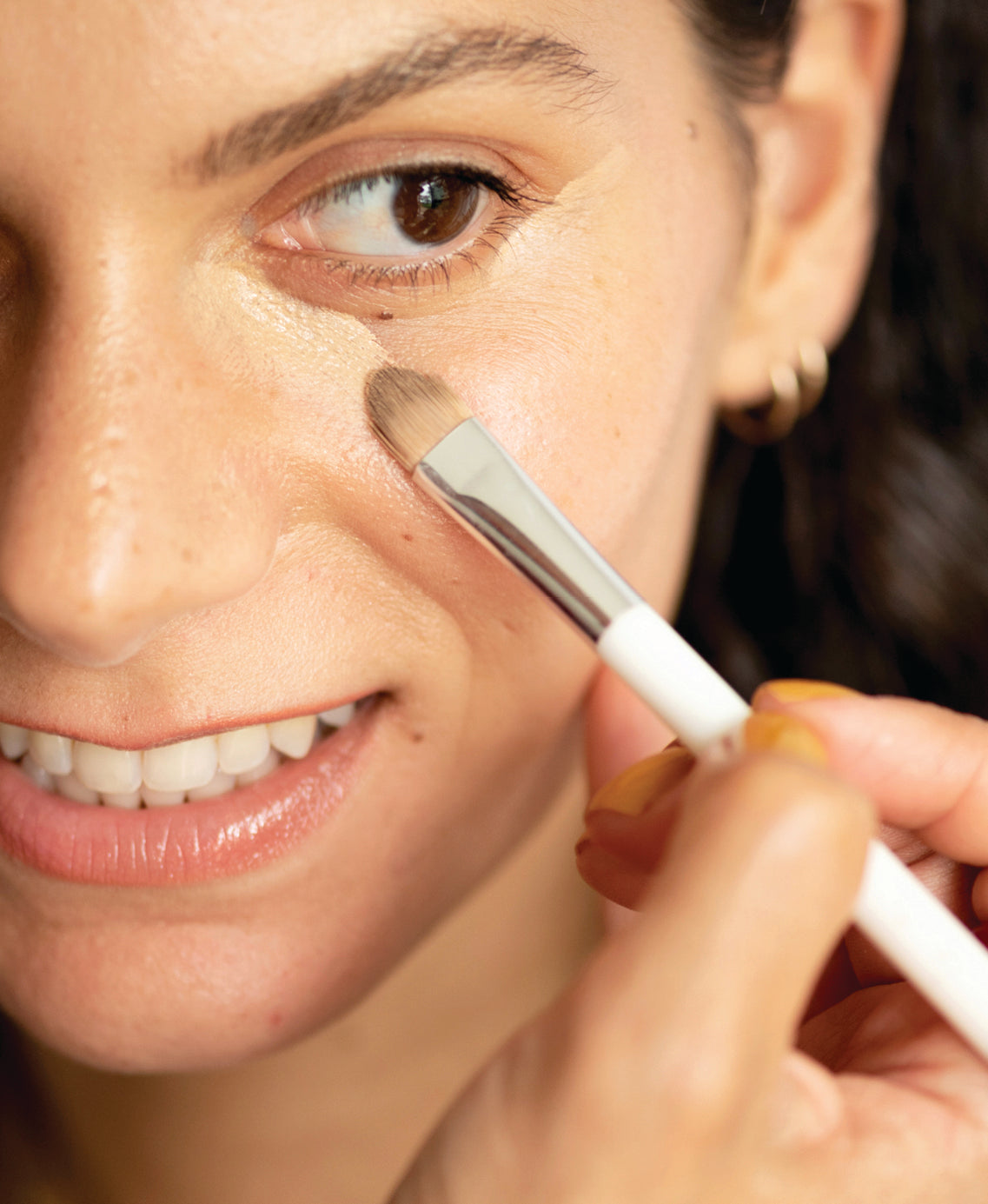 Model applying Ere Perez Lychee Creme Corrector beneath the eye with a brush
