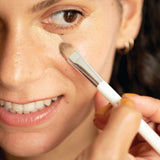 Model applying Ere Perez Lychee Creme Corrector beneath the eye with a brush