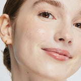Close-up portrait of a woman wearing Ere Perez Oat Milk Foundation in Nougat, with an even light-beige complexion, faint freckles across her cheeks and softly glossy pink lips.